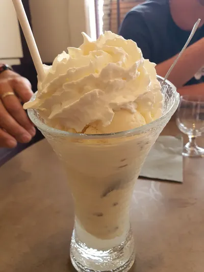 Coupe glacée à la vanille couronnée d'une généreuse chantilly, servie dans un verre haut avec paille et longue cuillère.