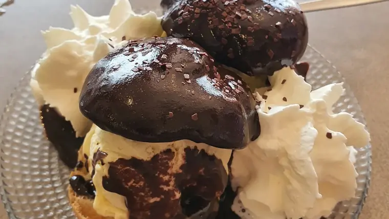 Profiteroles au chocolat : choux garnis de glace vanille, nappés de chocolat chaud brillant, avec de la chantilly.