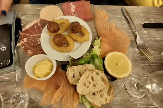 Planche à partager sur plateau de verre : saumon fumé, charcuteries, croquettes, oignons frits, salade, citron et pain grillé.