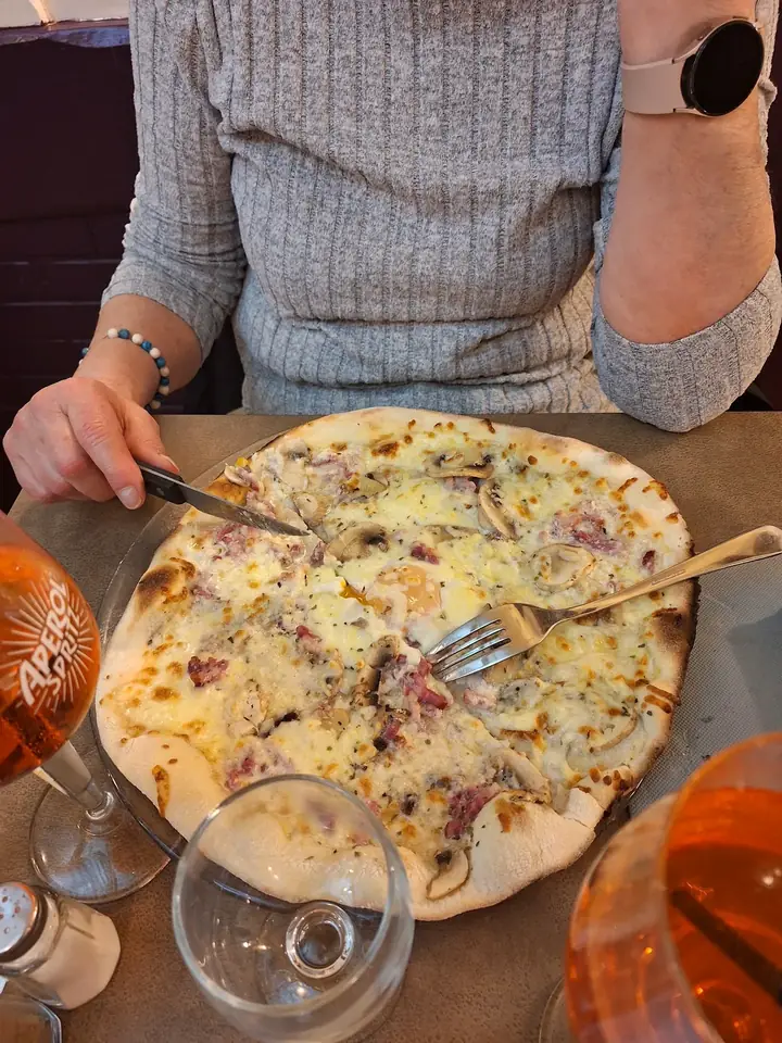 Pizza blanche à la crème, lardons, champignons et œuf, servie en salle au Pinocchio, découpée à table entre deux spritz.