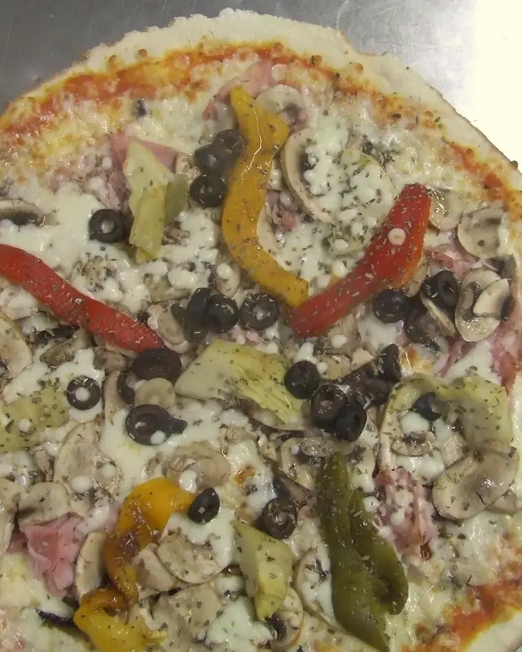 Pizza à pâte fine vue du dessus, garnie de jambon, champignons, artichauts, poivrons rouges et jaunes et olives noires.