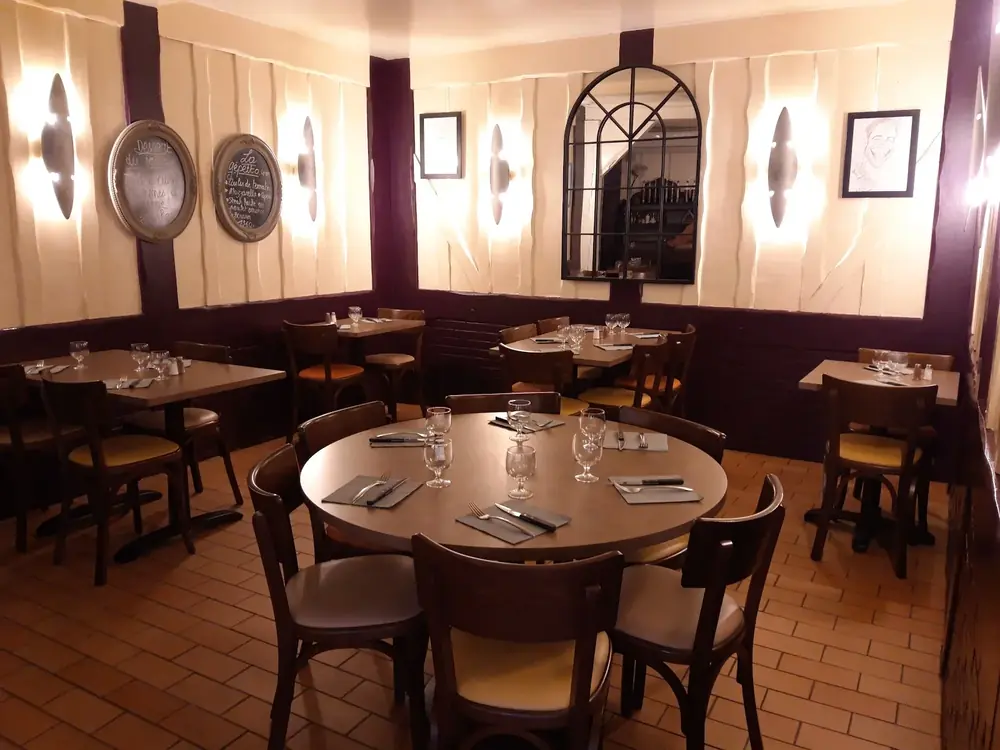 Salle du Pinocchio : tables dressées, chaises bistrot à assise jaune, colombages bordeaux, toiles murales crème, tomettes au sol et ardoises ovales accrochées au mur.