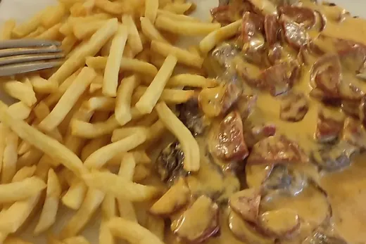 Pièce de bœuf nappée d'une sauce crémeuse au chorizo, servie avec des frites sur une assiette blanche.